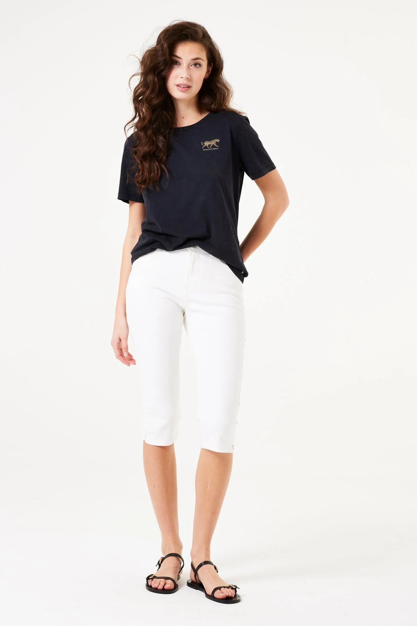 Front view of a woman wearing slim-fit capri pants paired with a short-sleeve top and flat sandals, showcasing the cropped silhouette.