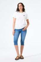 Woman wearing a fitted capri-length denim pant paired with a short-sleeve t-shirt and slide sandals, shown from the front.
