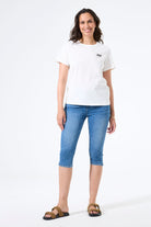 Woman wearing a fitted capri-length denim pant paired with a short-sleeve t-shirt and slide sandals, shown from the front.