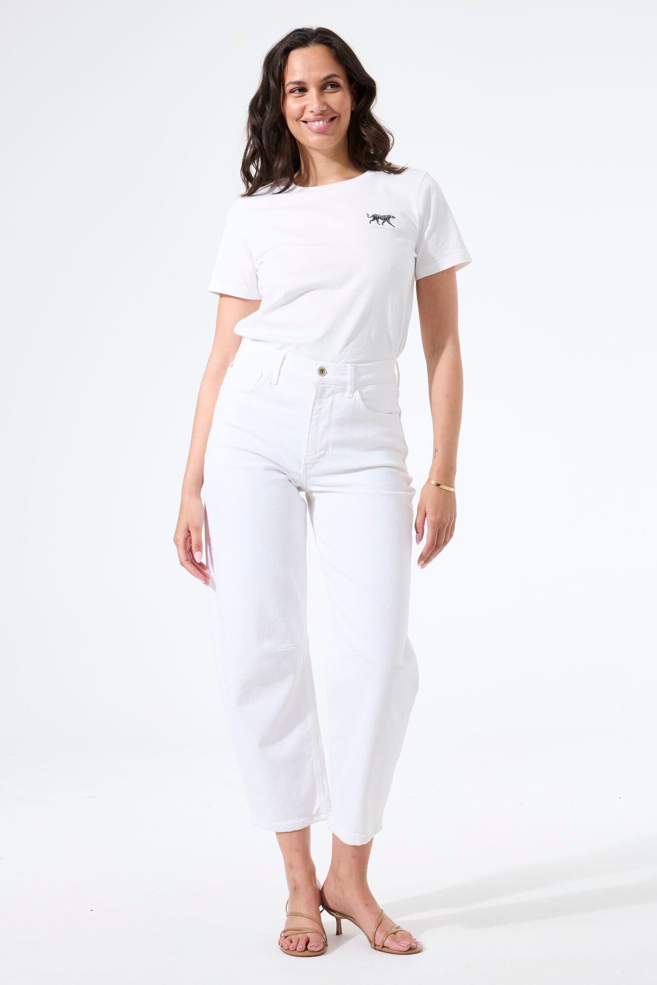 Model wearing white barrel-leg denim jeans with a fitted sleeveless top and heeled sandals, creating a casual, modern silhouette.