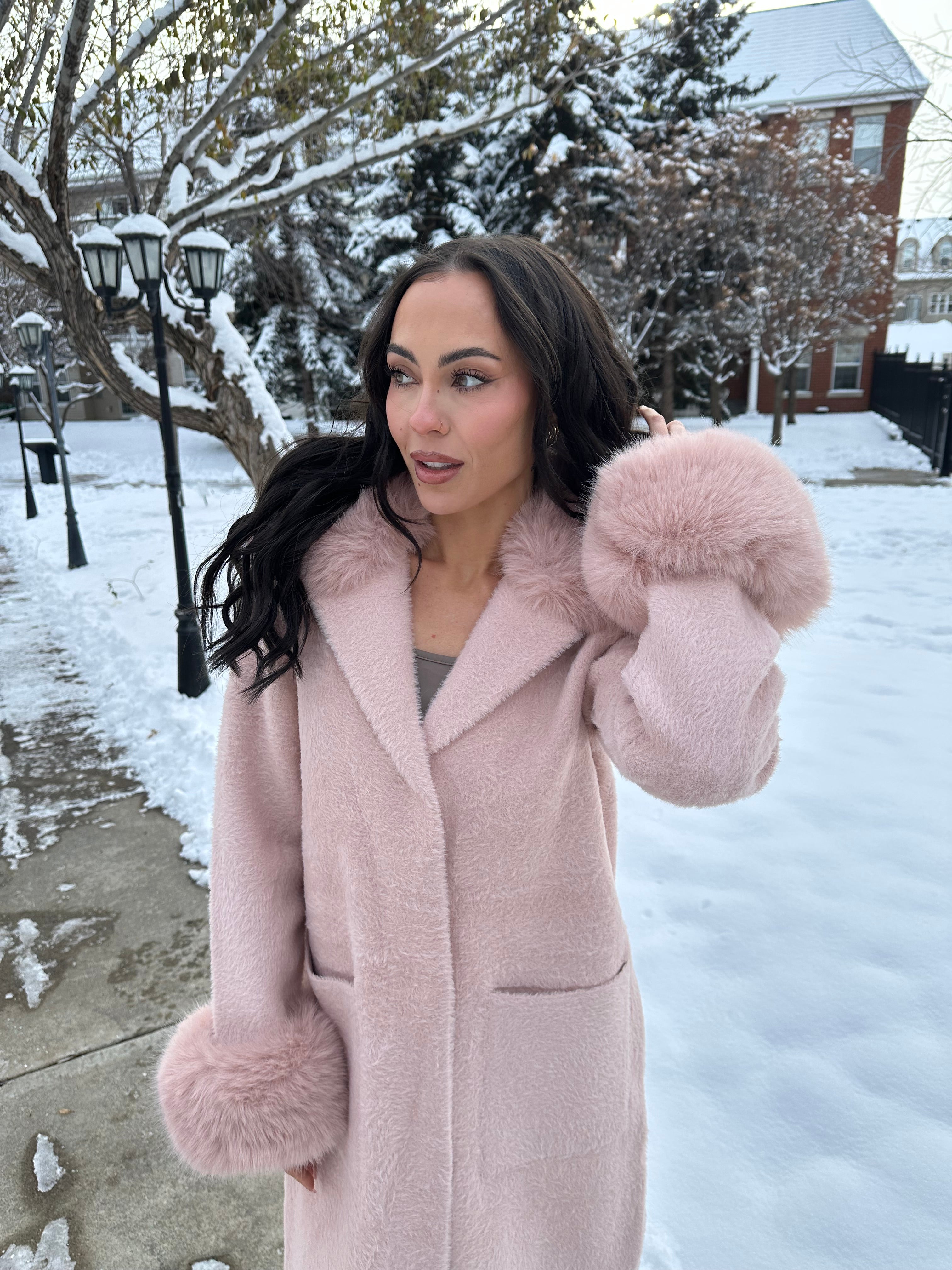 Woman wearing a soft pink Faux Fur Trim Coat in Feather Yarn with faux fur trim on sleeves, standing in winter scenery.
