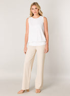 Women's white sleeveless blouse with a relaxed fit, round neckline, wide waistband hem, and soft draped silhouette, paired with cream wide-leg pants.