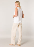 Women's white sleeveless blouse with a relaxed drape, wide waistband hem, and back keyhole detail, shown with cream wide-leg pants.