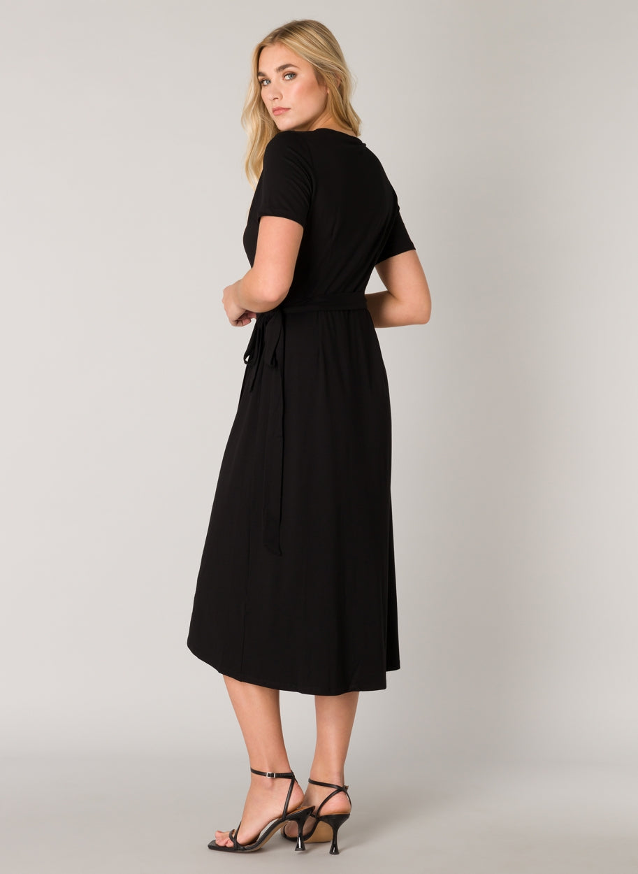 Women's black wrap midi dress shown from the back, featuring short sleeves, a self-tie waist belt, and a flowing midi-length skirt. The smooth fabric offers an effortless drape and comfortable fit.