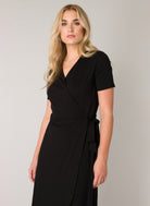 Close-up of a women's black wrap midi dress highlighting the V-neckline, wrap-front bodice, and side tie detail. The soft viscose-blend fabric provides a smooth finish with comfortable stretch.