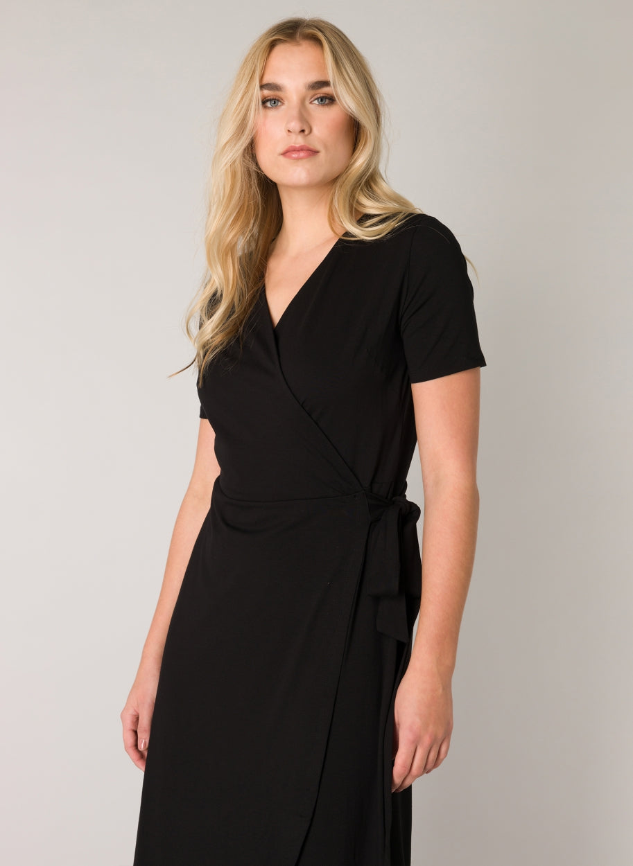 Close-up of a women's black wrap midi dress highlighting the V-neckline, wrap-front bodice, and side tie detail. The soft viscose-blend fabric provides a smooth finish with comfortable stretch.
