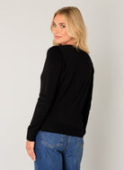 Women's black long-sleeve cardigan shown from the back, featuring a clean, minimalist design and a comfortable, relaxed fit. Styled with wide-leg blue jeans.