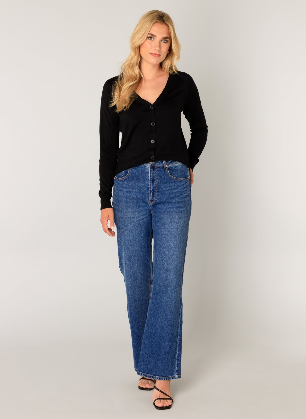 Women's black button-front cardigan with a V-neckline and long sleeves, shown from the front. Styled with wide-leg blue jeans and strappy sandals for a casual, polished look.