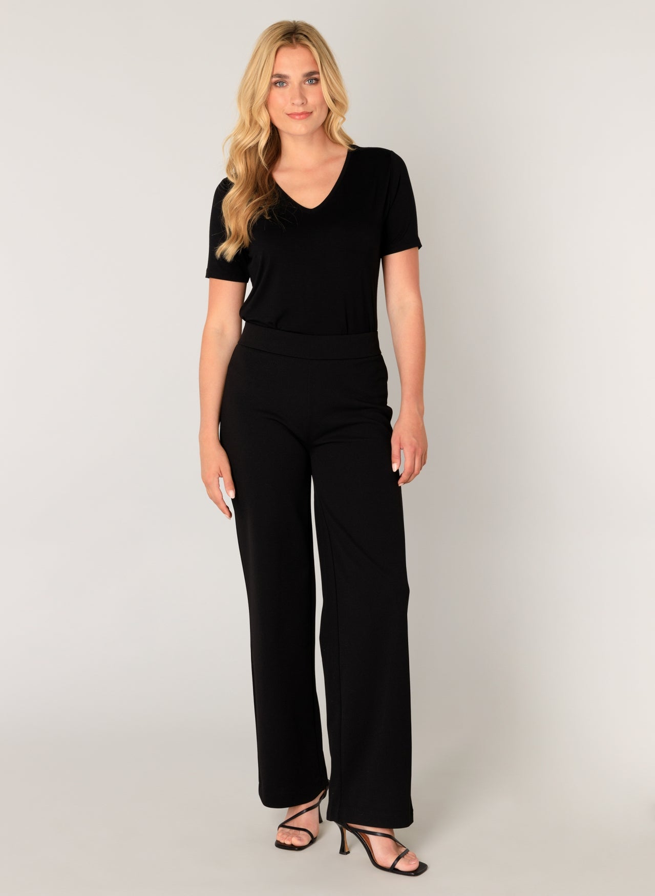 Model wearing black wide-leg knit pants with a pull-on waistband and matching short-sleeve top. The relaxed silhouette and soft stretch fabric create an effortless, polished look.