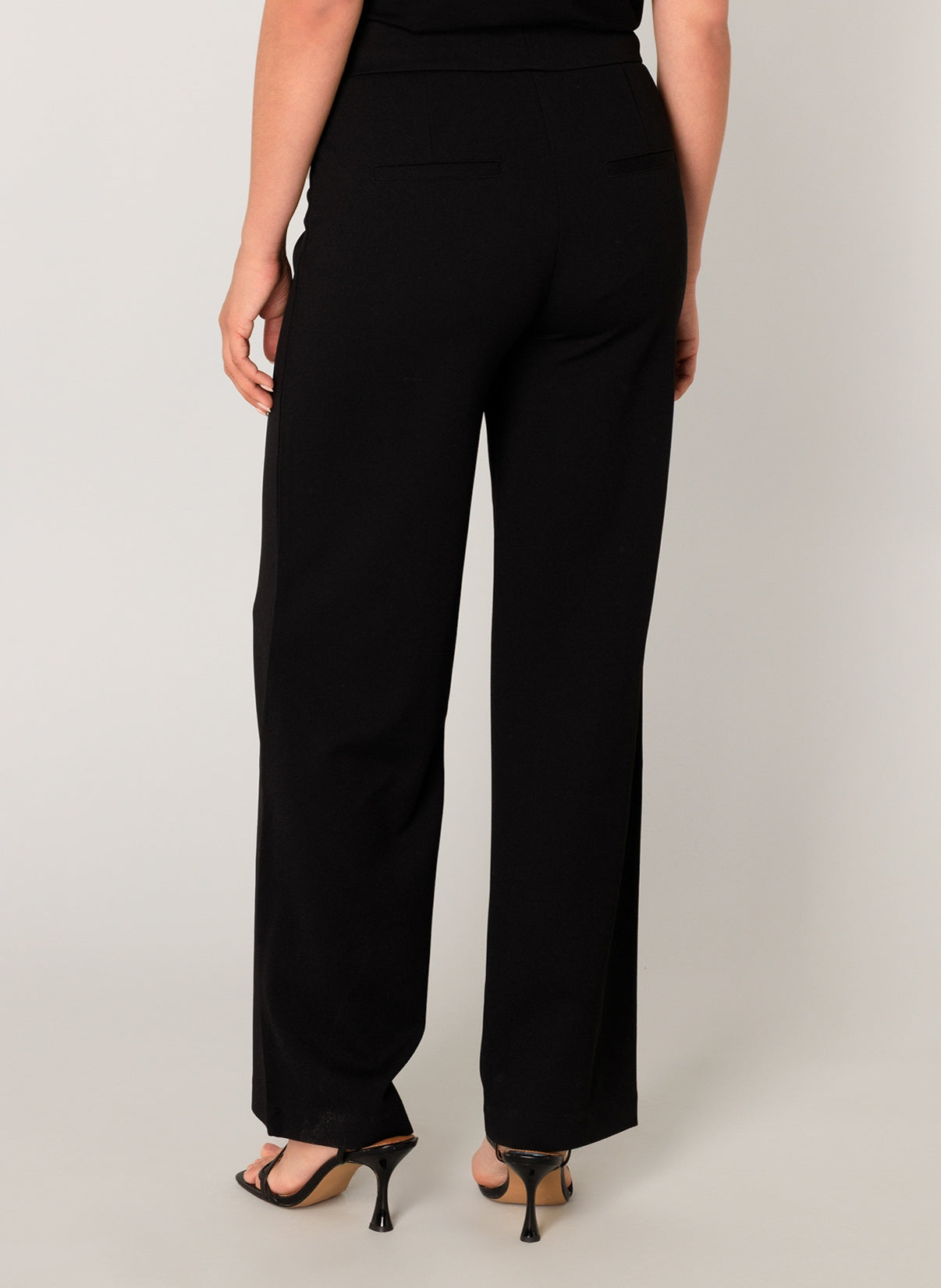Women's black wide-leg knit pants featuring a smooth pull-on waistband, relaxed straight silhouette, and faux welt back pockets. Styled with heeled sandals, shown from the back.