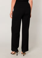 Women's black wide-leg knit pants featuring a smooth pull-on waistband, relaxed straight silhouette, and faux welt back pockets. Styled with heeled sandals, shown from the back.