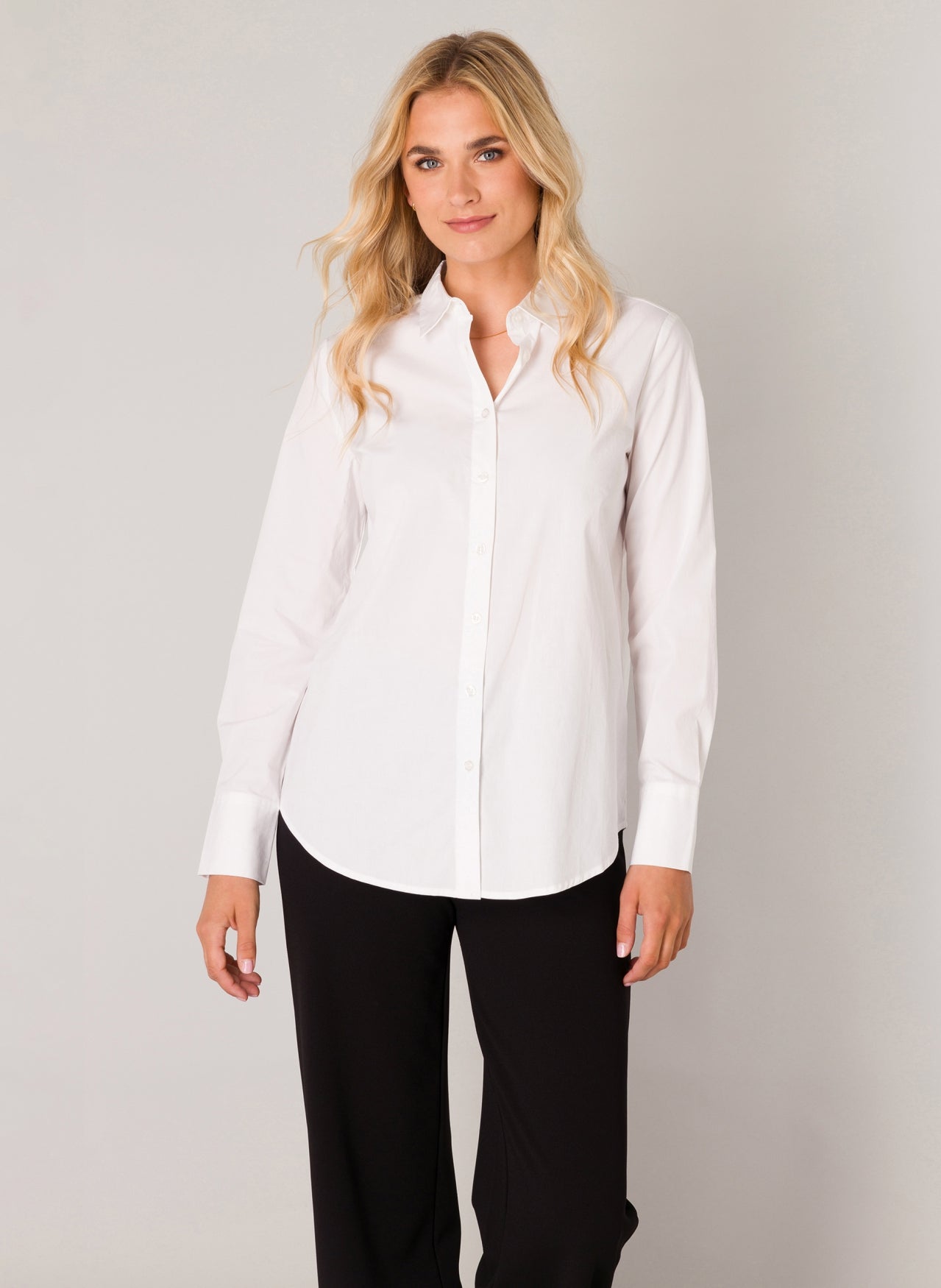 Woman wearing a white button-up shirt with a classic collar, long sleeves, and a relaxed silhouette, styled with black pants for a polished everyday look.