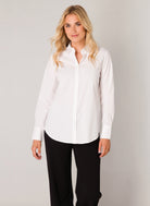 Woman wearing a white button-up shirt with a classic collar, long sleeves, and a relaxed silhouette, styled with black pants for a polished everyday look.