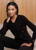 Woman wearing a black outfit with gold buttons against a wooden background