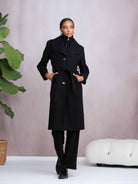 Woman wearing a black coat standing against a plain background