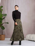 Woman wearing a black turtleneck and leopard print skirt standing against a plain background.