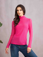 Woman wearing a bright pink turtleneck and blue jeans against a plain background