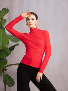 Woman wearing a red long-sleeve top and black pants against a gray background