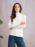 Woman wearing a white turtleneck and blue jeans against a gray background