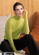 Woman in a green sweater sitting on a brown leather couch with a wooden wall background