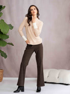 Woman wearing a beige sweater and brown pants standing against a plain background