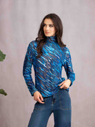 Woman wearing a blue patterned long-sleeve top and jeans against a gray background