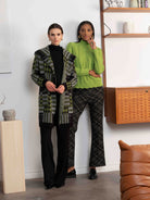 Two women standing in a room with a wooden shelf and brown leather chair.