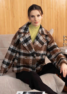 Woman wearing a plaid jacket sitting on a couch in a living room setting.