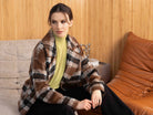 Woman wearing a plaid coat sitting on a couch with a wooden wall background