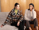Two women sitting on a couch, one wearing a plaid jacket and the other in a white sweater.