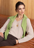 Woman sitting on a brown leather couch wearing a green vest and gray outfit.