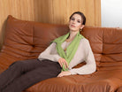 Woman sitting on a brown leather couch wearing a green scarf