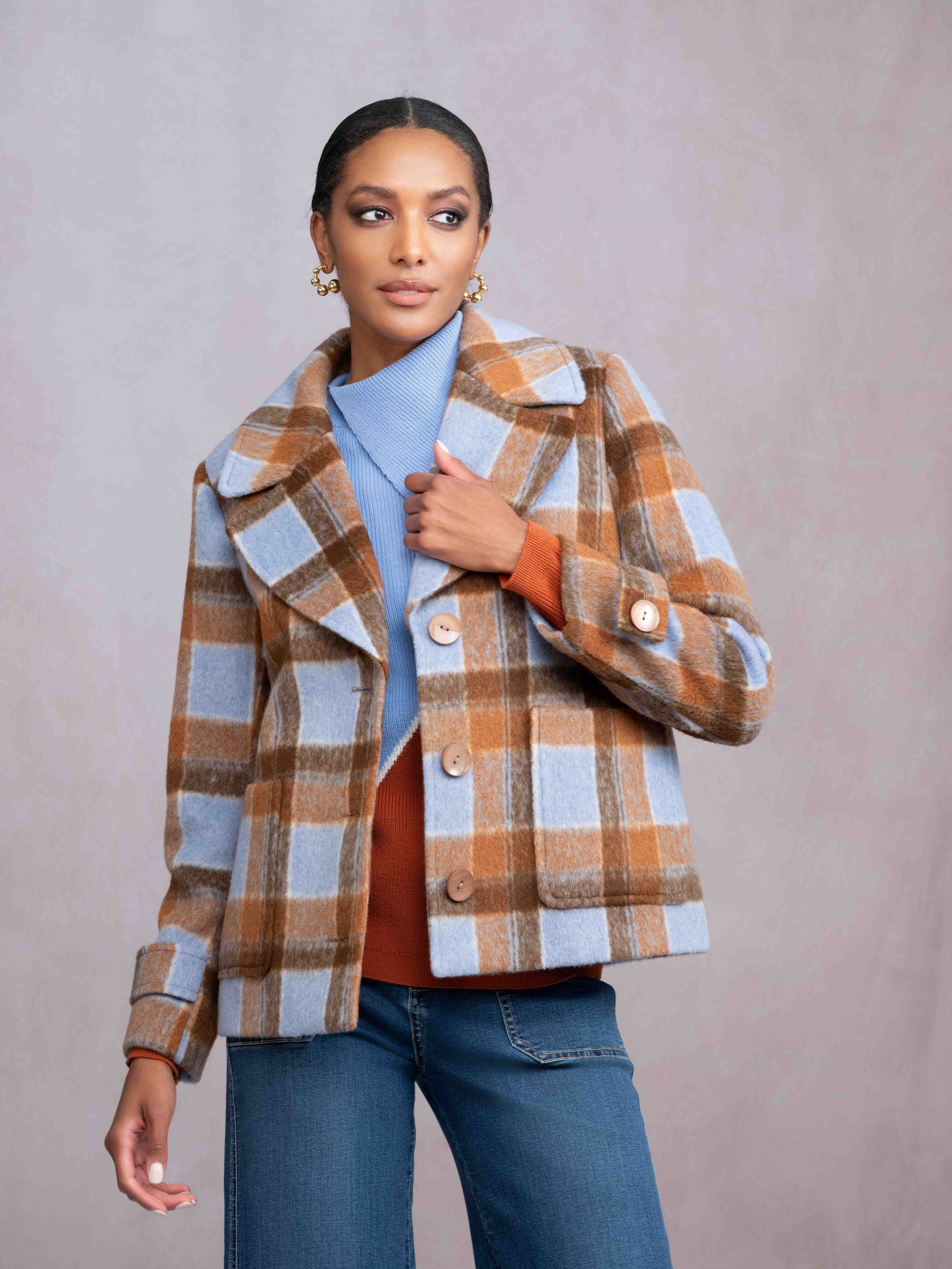 Woman wearing a plaid jacket over a blue shirt and orange sweater on a plain background
