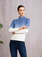 Woman wearing a two-tone blue and white sweater with dark jeans against a plain background