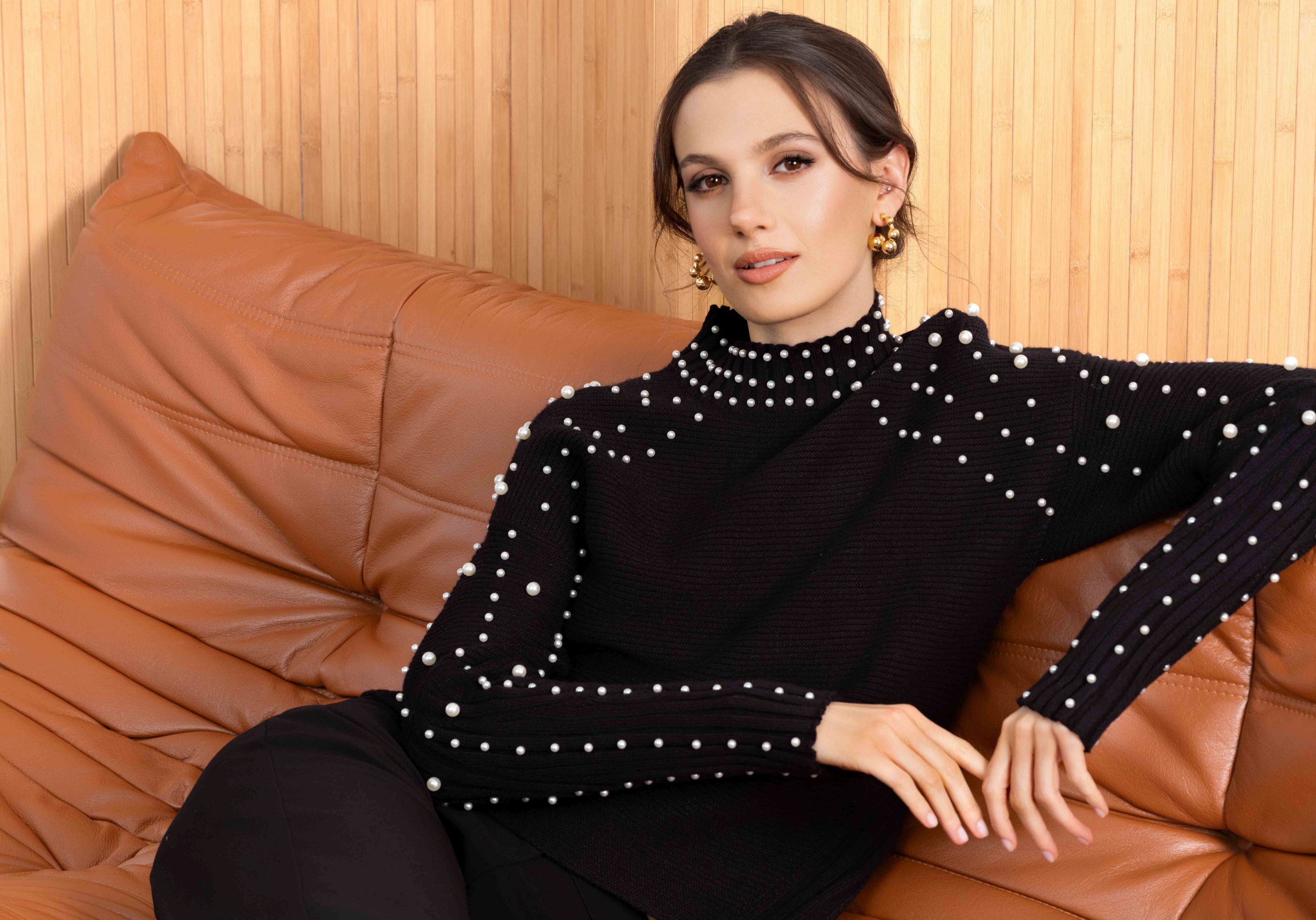 Woman wearing a black sweater with white polka dots sitting on a brown leather couch.