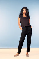 Woman wearing a black sleeveless top and pants against a blue background