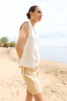 Woman in a white sleeveless top and yellow shorts standing on a sandy path with a clear sky.