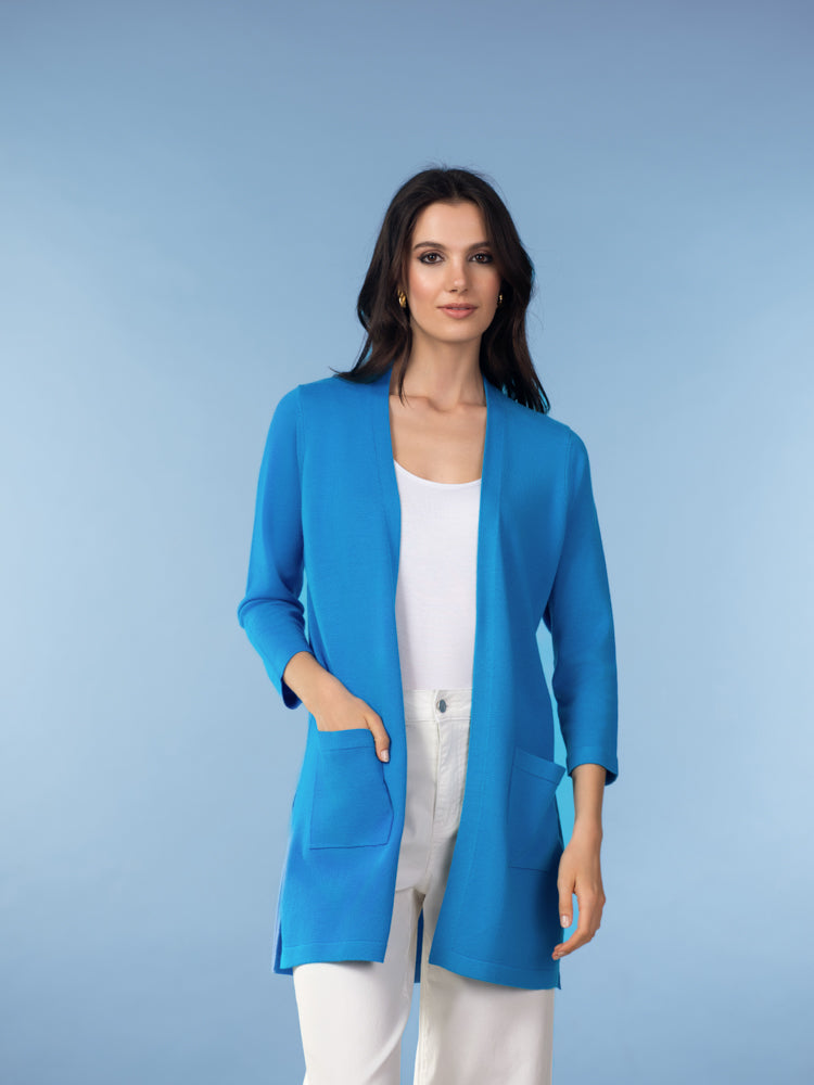 Woman wearing an open-front cardigan jacket with three-quarter sleeves and front patch pockets, styled over a sleeveless top and straight-leg trousers. The garment is shown from the front to highlight its drape, length, and clean, streamlined silhouette.
