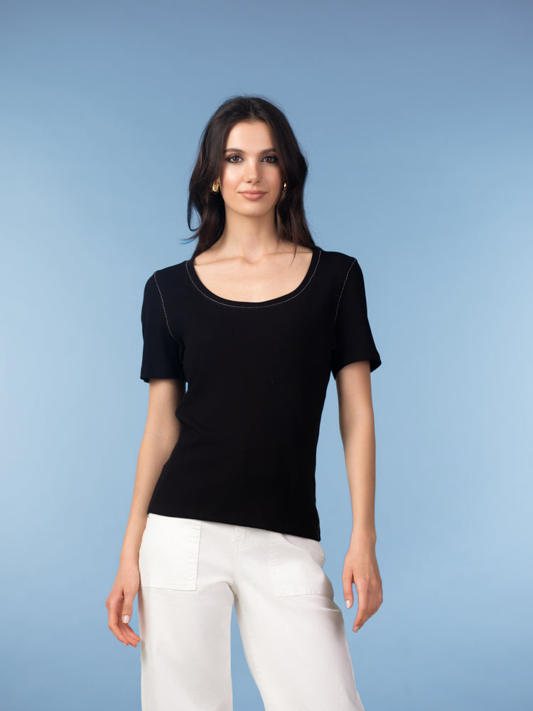 Women's short-sleeve knit t-shirt worn with white pants in a studio setting with a close-up view of the neckline, fit, and soft fabric texture. 