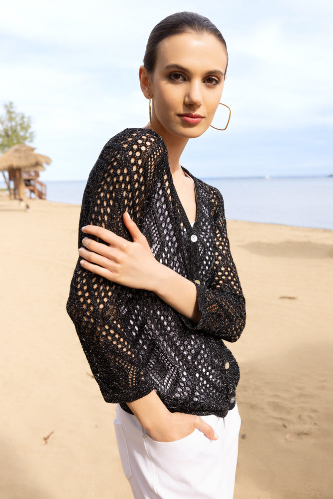 Model wearing an open-knit button-front cardigan styled casually, photographed outdoors at the beach with a relaxed, resort-inspired feel.