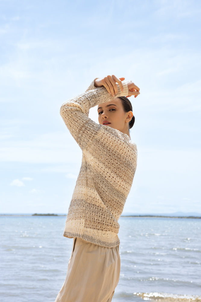 Side view of a model wearing a women’s lightweight open-knit pullover sweater with long sleeves, styled casually and photographed by the water.