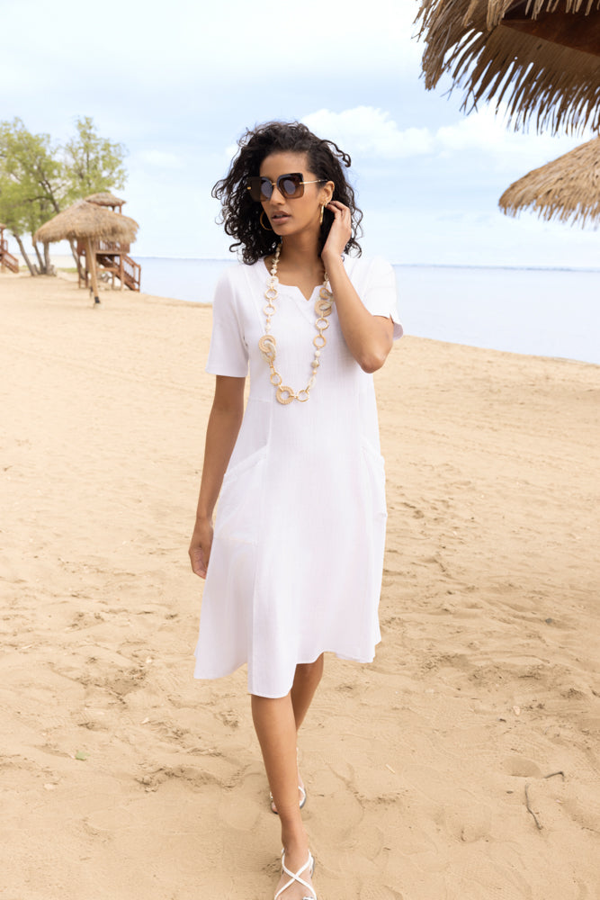 Woman in a white dress standing on a sandy beach with palm trees in the background