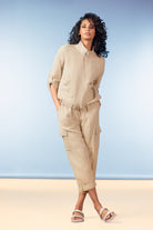 Woman wearing a beige outfit with cargo pants against a blue background