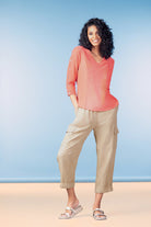 Woman wearing a coral top and beige pants against a blue background