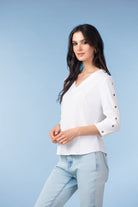 Woman wearing a white blouse with rolled-up sleeves and light blue jeans on a light blue background