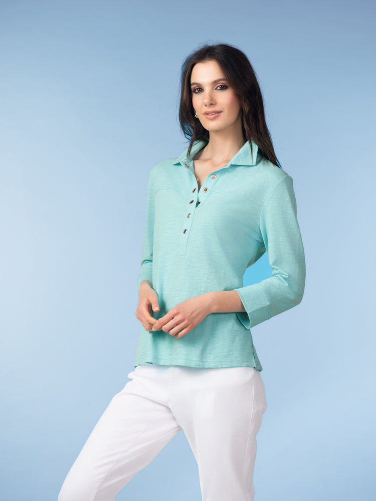 Model wearing a aqua cotton henley blouse with three-quarter sleeves and button-front neckline, styled with white pants against a light blue studio background.