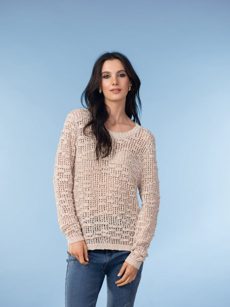Model wearing a beige open-knit crewneck sweater with long sleeves and ribbed trim, paired with blue jeans, studio background.