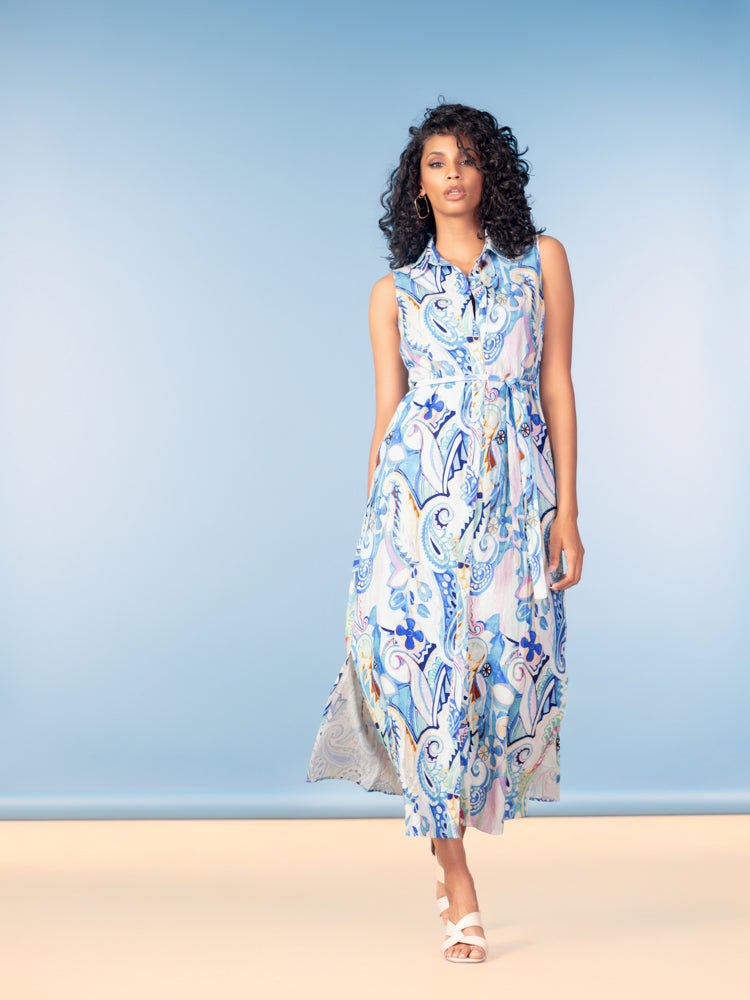 Sleeveless midi dress in a blue and ivory paisley print, crafted from a lightweight linen blend. Features a collared neckline, button-front bodice, defined waist, and flowing A-line skirt. Styled with neutral strappy heels against a soft blue backdrop.