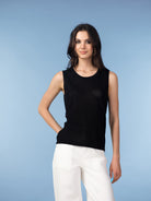 Model wearing a black sleeveless knit tank featuring a clean neckline and straight silhouette, paired with light beige tailored trousers in a studio setting.