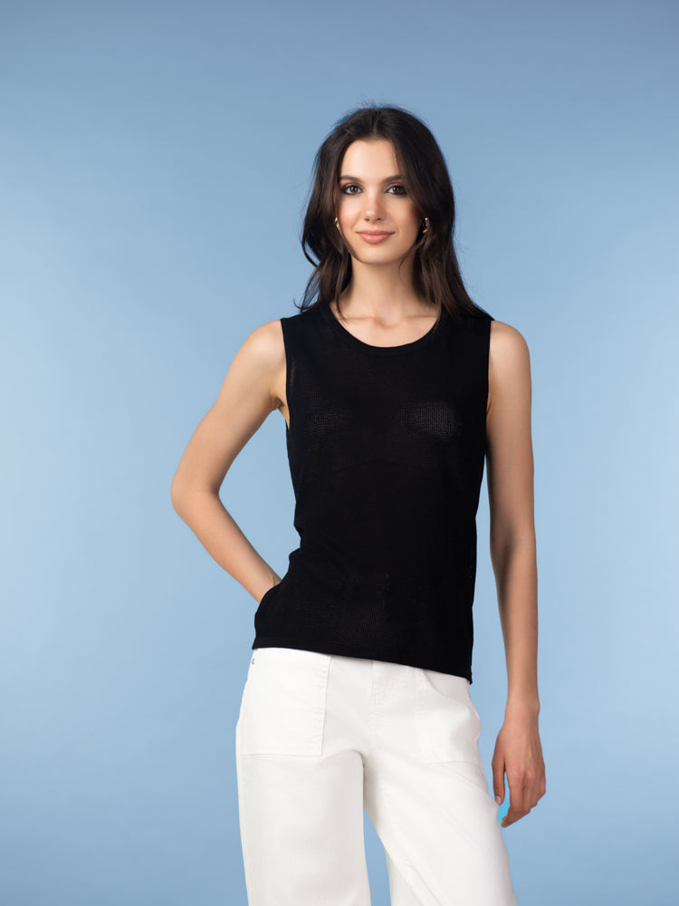 Model wearing a black sleeveless knit tank featuring a clean neckline and straight silhouette, paired with light beige tailored trousers in a studio setting.